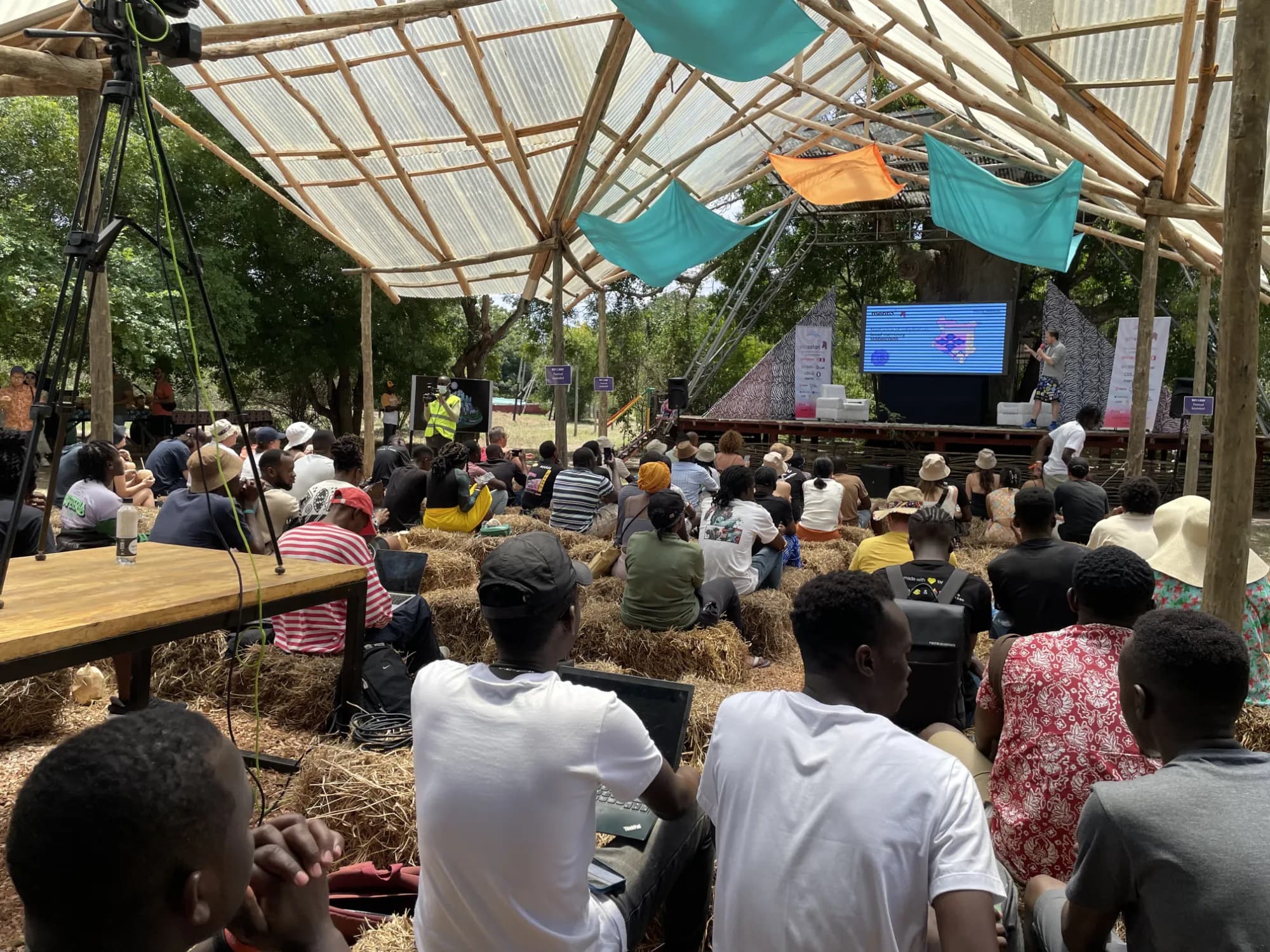 An outdoor festival crowd seated on hay bales for a stage session